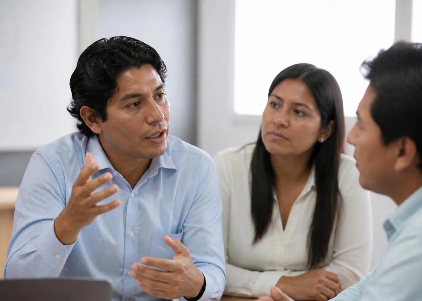 Tres profesionales en una sala de reuniones clara, uno de ellos explicando