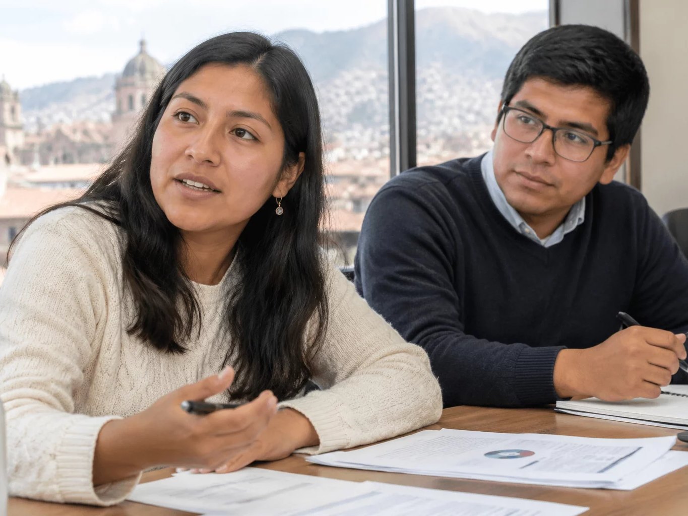 Dos adultos en una mesa de trabajo cubierta de apuntes impresos